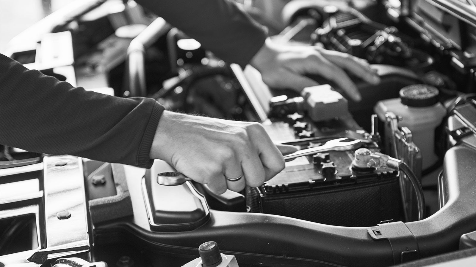 An up-close shot of someone working on a vehicle underneath the hood